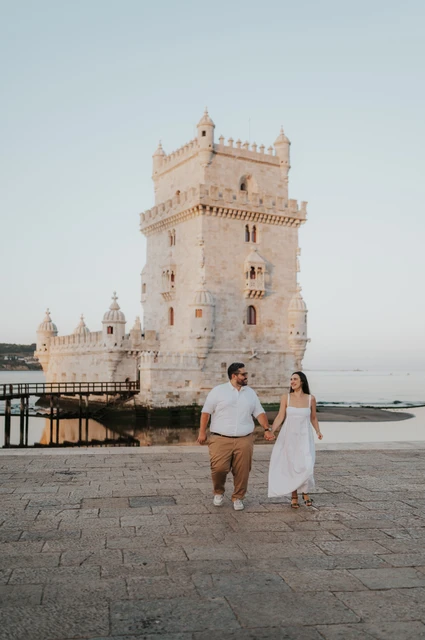A shared glance during their waterfront walk | Lisbon anniversary photoshoot The couple looking at each other while walking hand in hand in front of Belém Tower during their anniversary photoshoot in Lisbon.