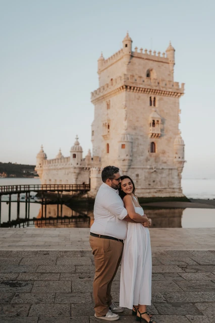 A smiling embrace by Belém Tower | Lisbon anniversary photoshoot The man embracing his smiling partner from the side with Belém Tower behind them during their anniversary photoshoot in Lisbon.