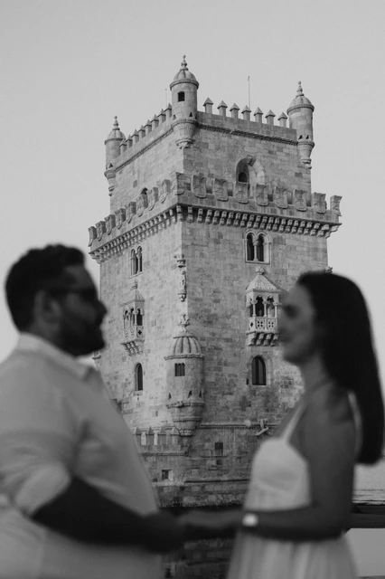 A soft tower portrait in black and white | Lisbon anniversary photoshoot A softly focused black-and-white portrait of the couple with Belém Tower sharp in the background during their anniversary photoshoot in Lisbon.
