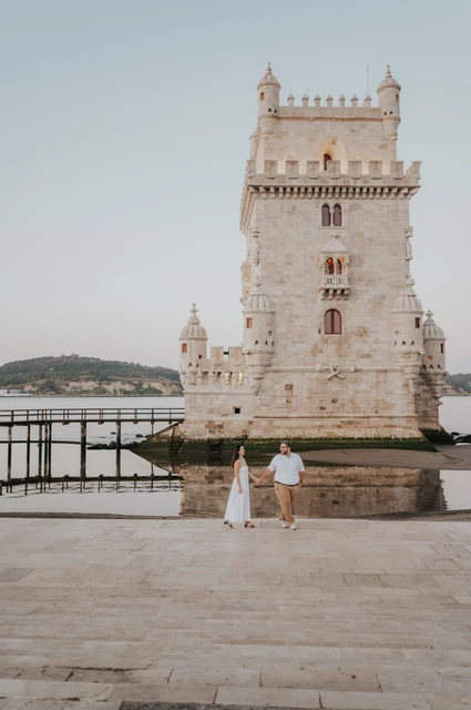 A full tower view above the couple | Lisbon anniversary photoshoot A wide vertical portrait of the couple holding hands with Belém Tower above them during their anniversary photoshoot in Lisbon.