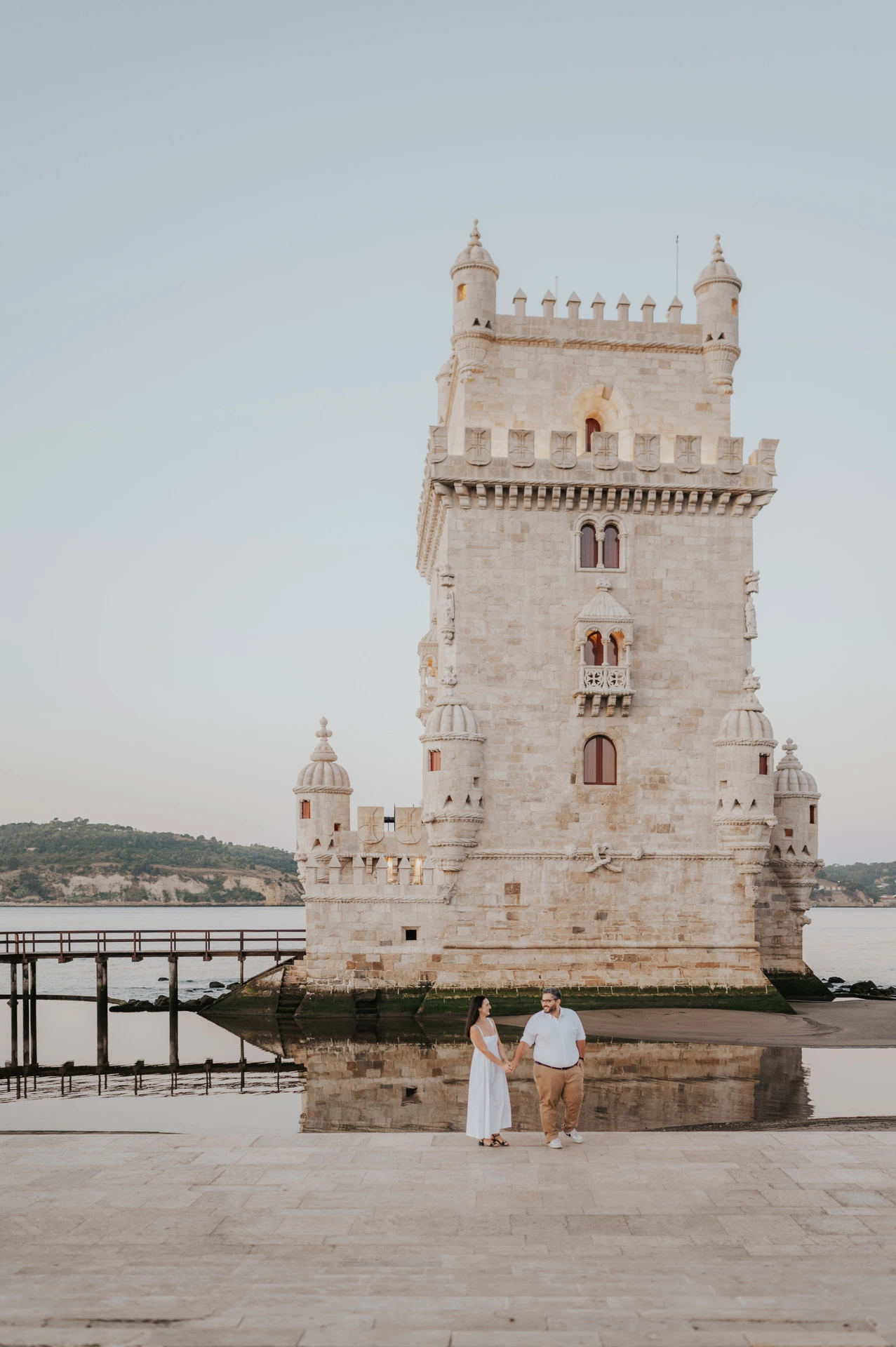 The couple standing together on the stone waterfront beneath Belém Tower during their anniversary photoshoot in Lisbon.