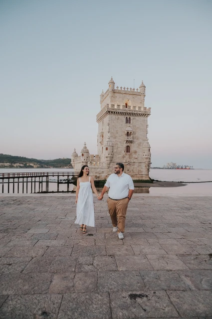Hand in hand across the paving | Lisbon anniversary photoshoot A full-length view of the couple walking hand in hand across the stone paving by Belém Tower during their anniversary photoshoot in Lisbon.