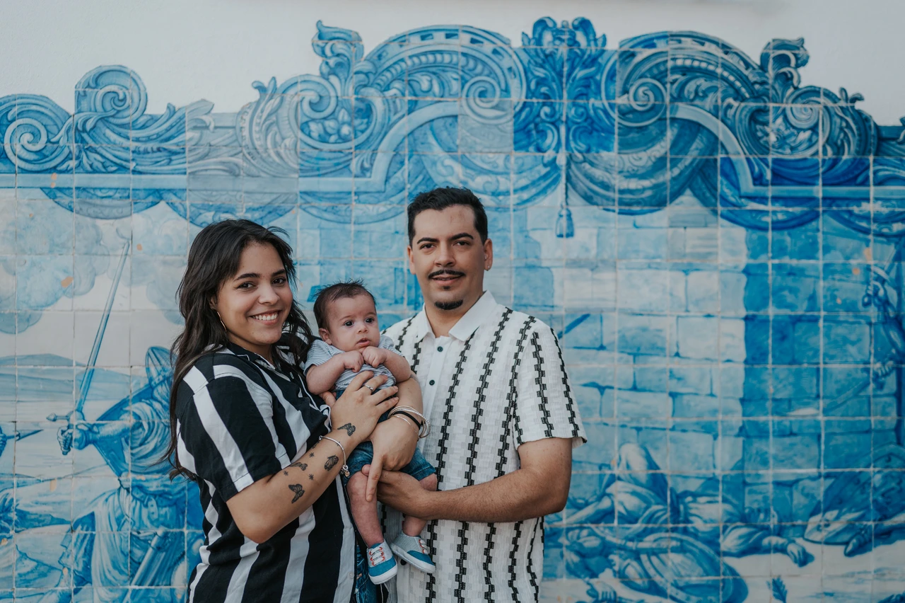 A family portrait against the blue tiles | Lisbon family photoshoot The parents holding their baby in front of a blue-and-white Portuguese tile panel during their family photoshoot in Lisbon.