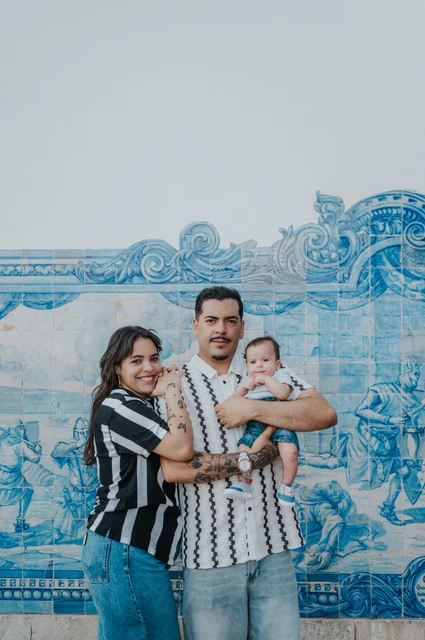 A family portrait against the blue tiles | Lisbon family photoshoot The parents holding their baby in front of a blue-and-white Portuguese tile panel during their family photoshoot in Lisbon.