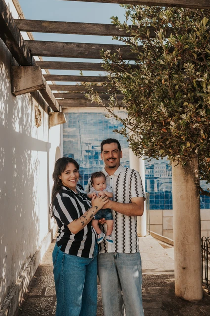 The parents holding their baby beneath the pergola at Miradouro de Santa Luzia during their family photoshoot in Lisbon.