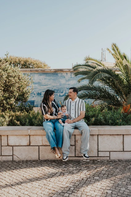 Seated together beside the palms | Lisbon family photoshoot The parents seated together holding their baby beside palm leaves and blue Portuguese tiles during their family photoshoot in Lisbon.