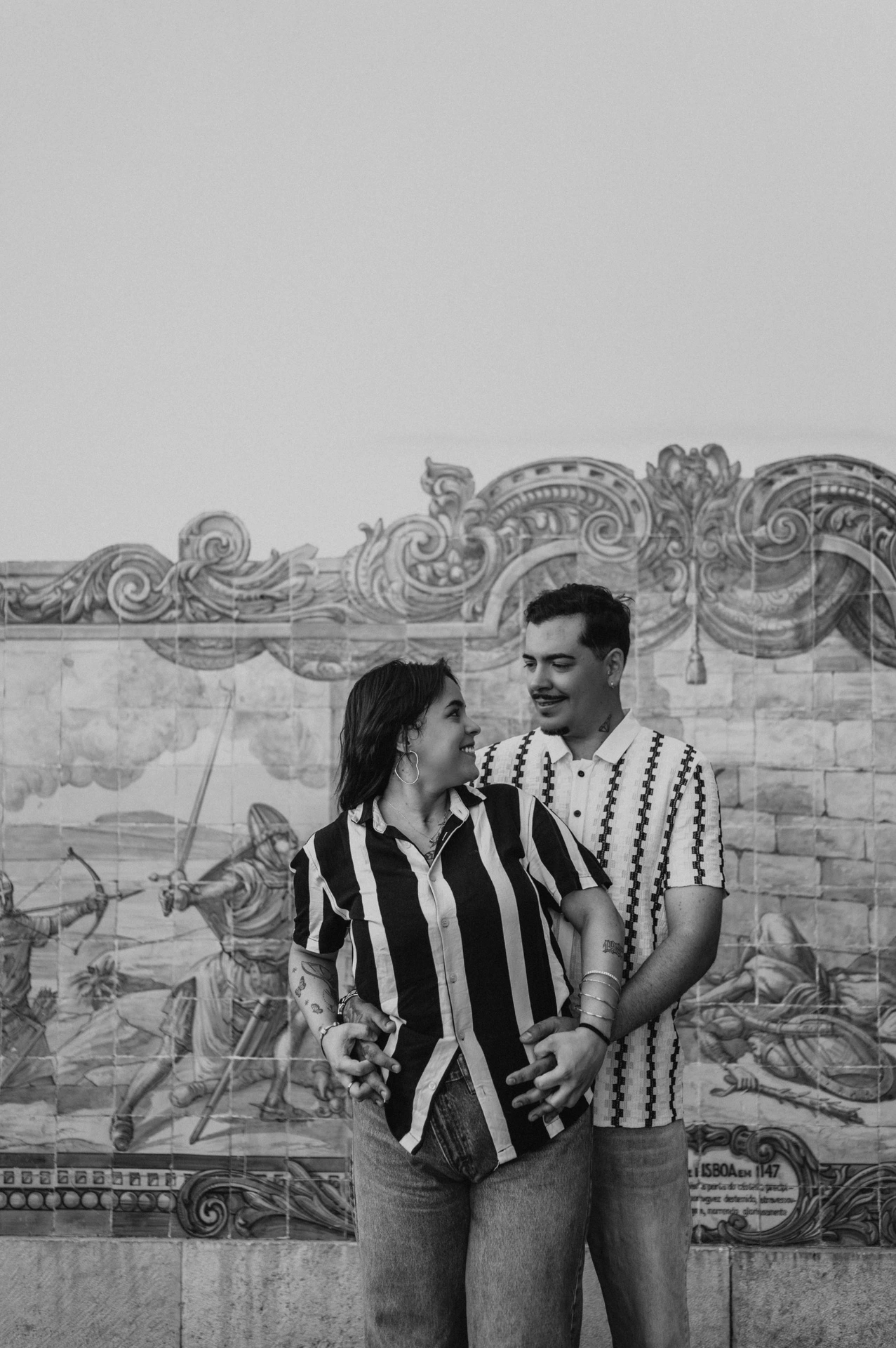 Black-and-white photograph: the parents smiling at each other in a close embrace against the blue tile panel during their family photoshoot in Lisbon.