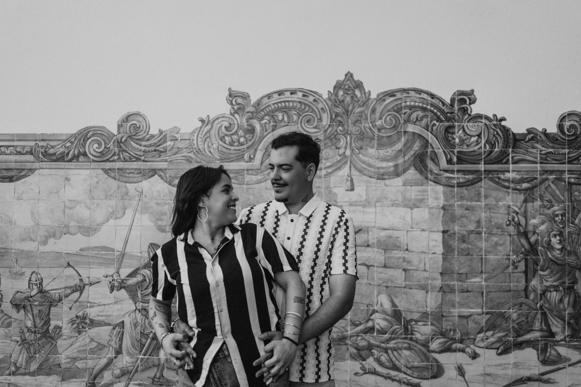 Black-and-white photograph: the parents smiling at each other in a close embrace against the blue tile panel during their family photoshoot in Lisbon.