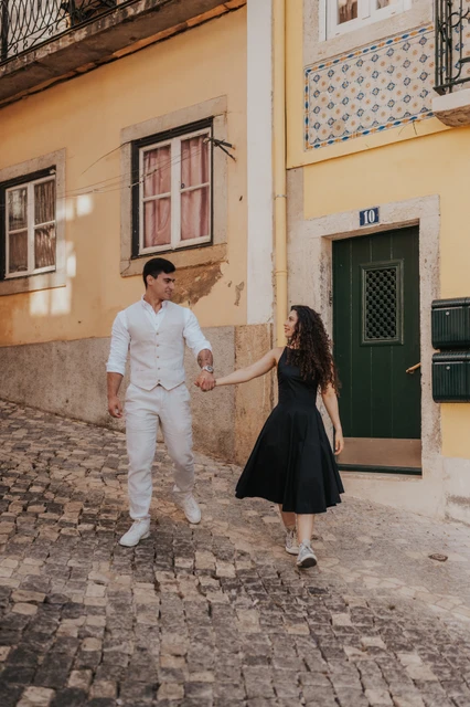 A walk along Bica’s cobbled street | Lisbon couple photoshoot The couple walking hand in hand along the cobbled street beside yellow façades during their couple photoshoot in Lisbon.