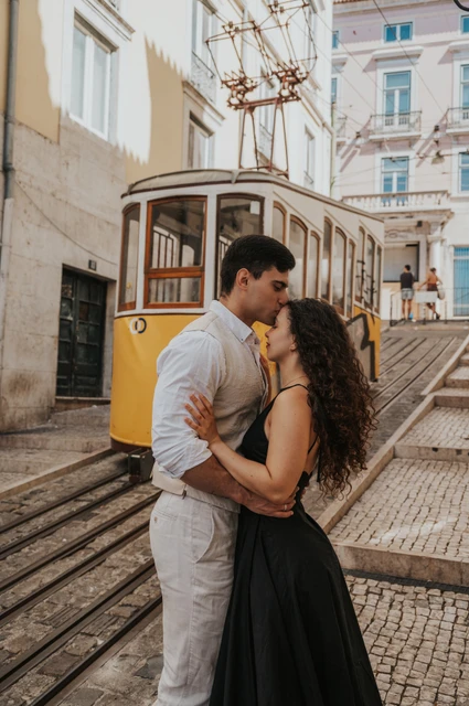A kiss beside the funicular | Lisbon couple photoshoot The couple kissing with a yellow funicular and the sloping street behind them during their couple photoshoot in Lisbon.