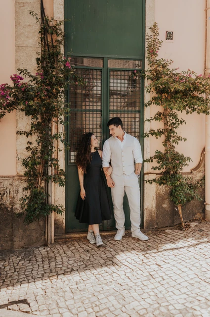 The couple smiling beside a green doorway framed by climbing plants during their couple photoshoot in Lisbon.