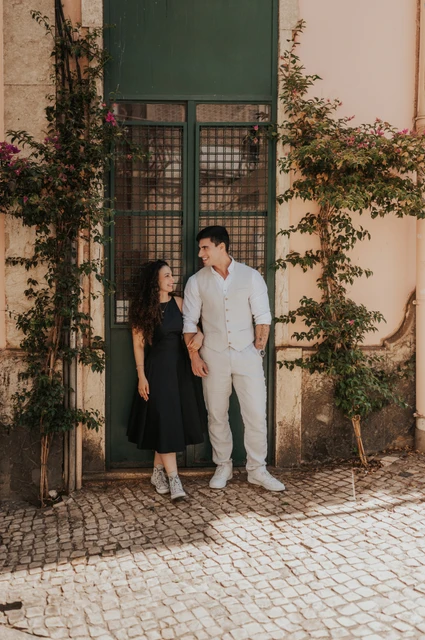 Together at the green doorway | Lisbon couple photoshoot The couple smiling beside a green doorway framed by climbing plants during their couple photoshoot in Lisbon.