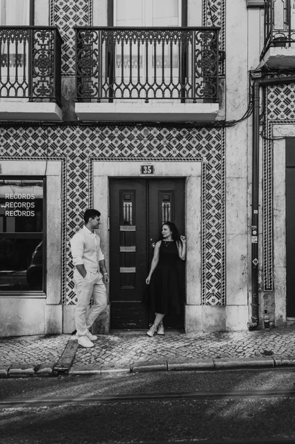 A portrait at the green tiled doorway in black and white | Lisbon couple photoshoot Black-and-white photograph: the couple standing apart beside a green door surrounded by patterned tiles during their couple photoshoot in Lisbon.
