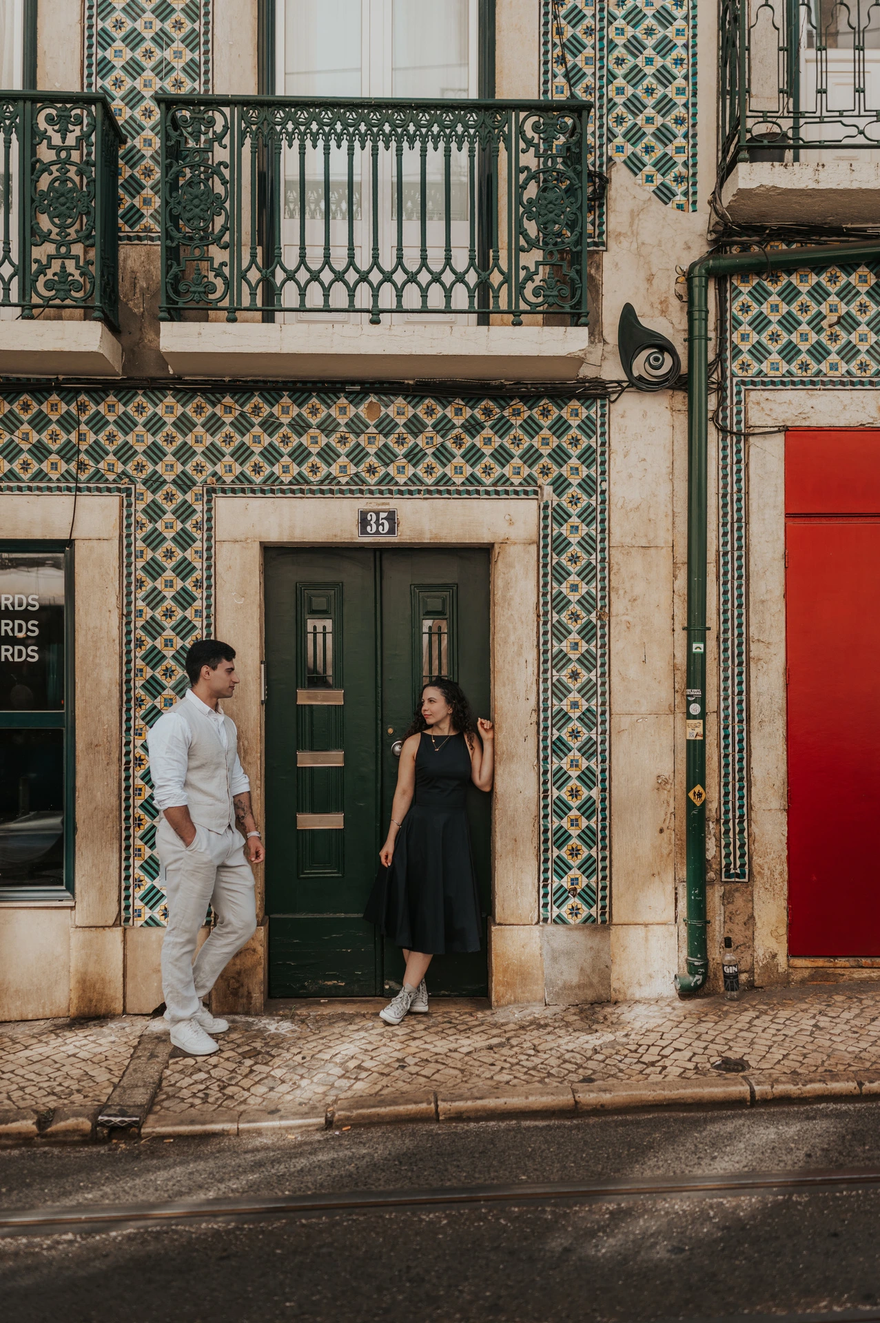 The couple standing apart beside a green door surrounded by patterned tiles during their couple photoshoot in Lisbon.