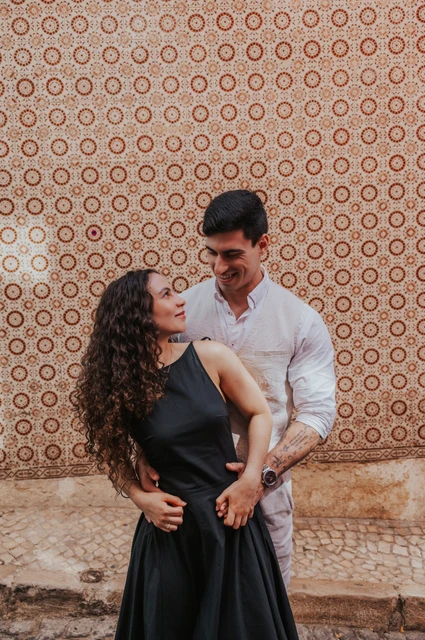 An embrace against the patterned tiles | Lisbon couple photoshoot The man embracing his partner from behind against the pink tile wall during their couple photoshoot in Lisbon.