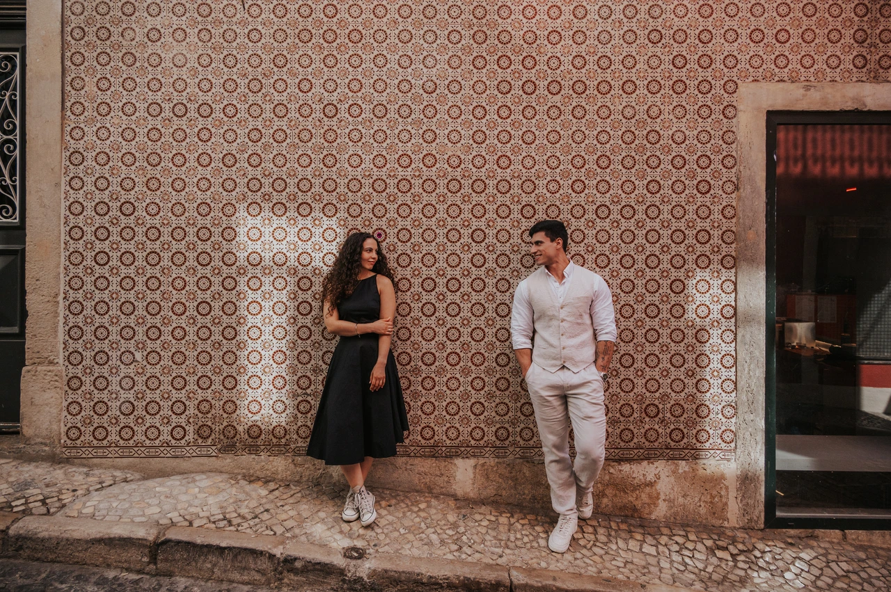Smiles beside the pink tiles | Lisbon couple photoshoot The couple smiling at each other while standing apart against a pink patterned tile wall during their couple photoshoot in Lisbon.