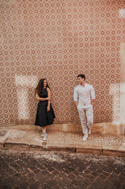 Smiles beside the pink tiles | Lisbon couple photoshoot The couple smiling at each other while standing apart against a pink patterned tile wall during their couple photoshoot in Lisbon.