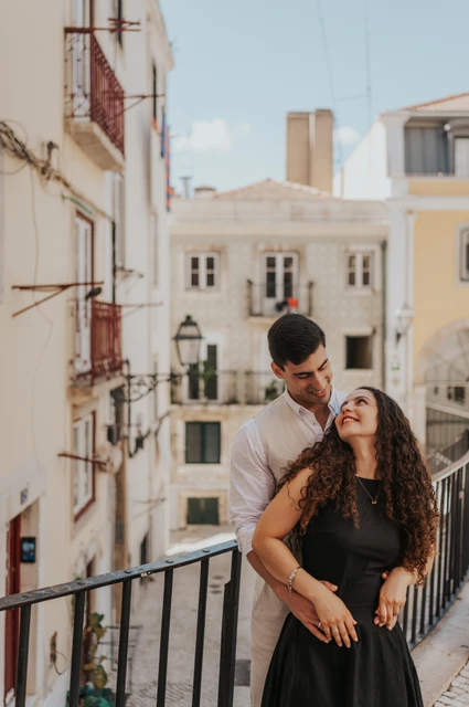 A close portrait above the old street | Lisbon couple photoshoot The man embracing his partner from behind beside a railing above the street during their couple photoshoot in Lisbon.