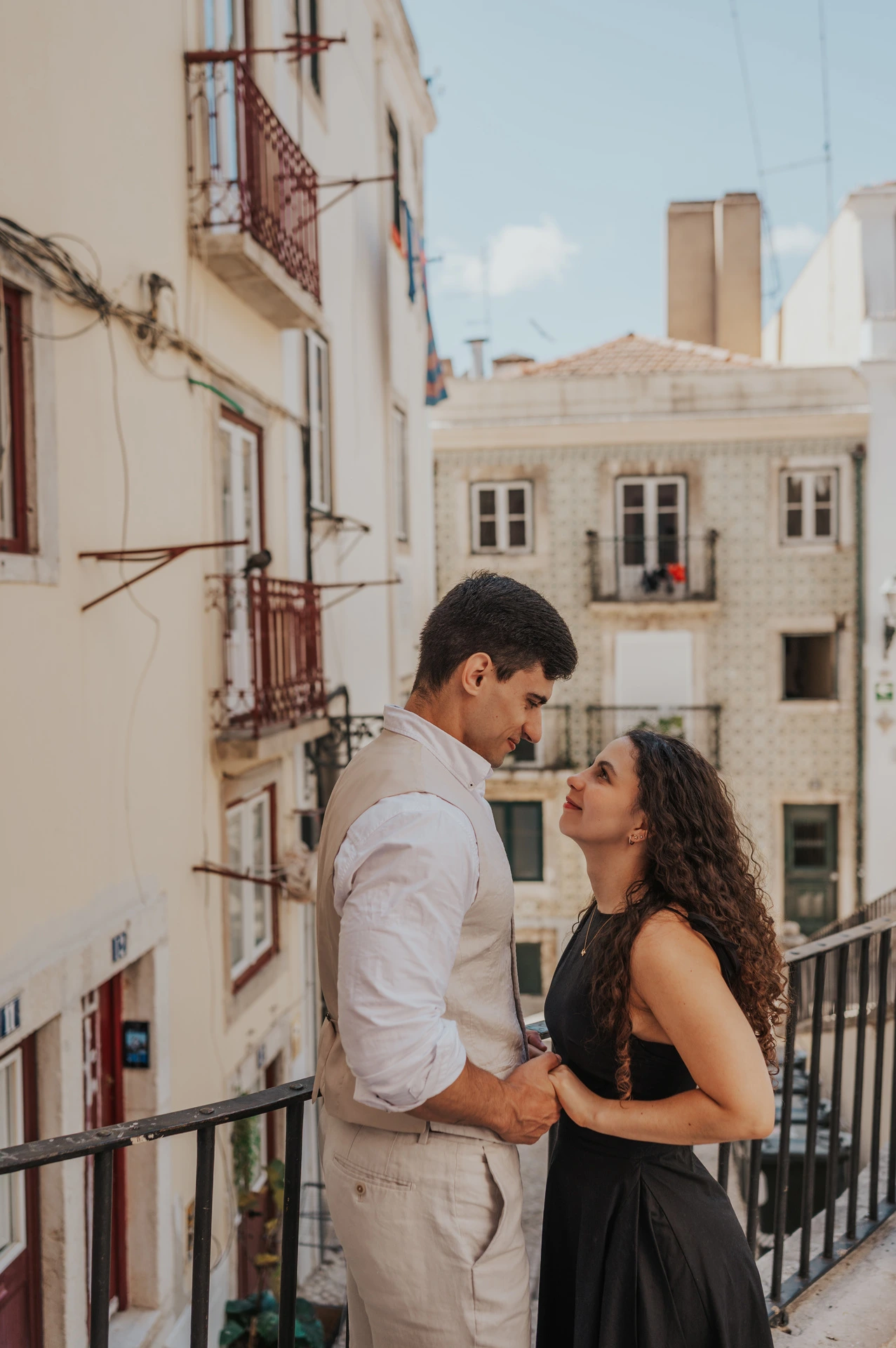 The couple facing each other and holding hands beside the street railing during their couple photoshoot in Lisbon.