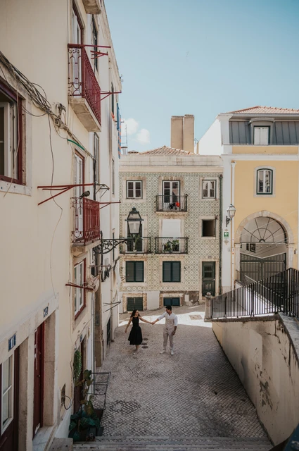 A wide view of the couple beside the railing with the old street and buildings below them during their couple photoshoot in Lisbon.
