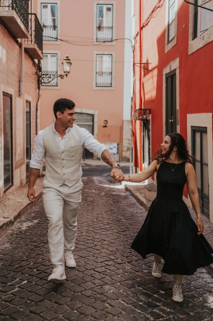 A smiling walk through the colourful street | Lisbon couple photoshoot The couple smiling and holding hands as they walk together along a narrow street with red façades during their couple photoshoot in Lisbon.