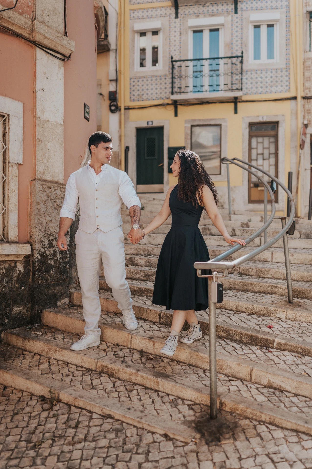 The couple holding hands while standing on the little stone steps beside the street during their couple photoshoot in Lisbon.