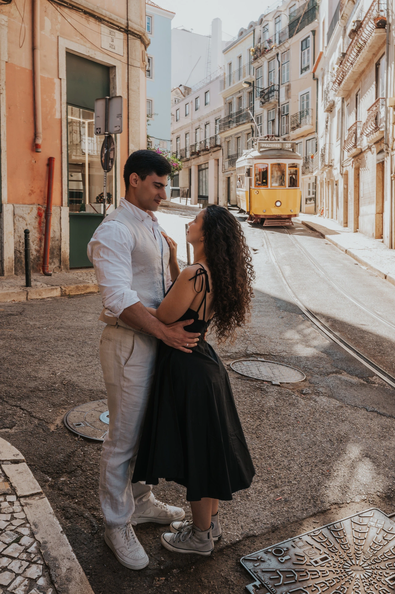 The couple embracing beside the street with the yellow funicular farther behind them during their couple photoshoot in Lisbon.