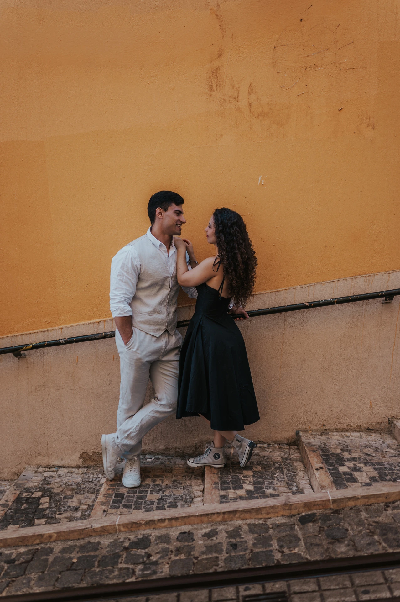 The couple embracing on the stone stairway beside a warm yellow wall during their couple photoshoot in Lisbon.