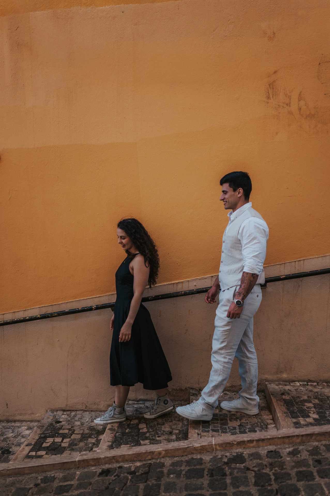 The couple descending the stone stairway beside the yellow wall during their couple photoshoot in Lisbon.