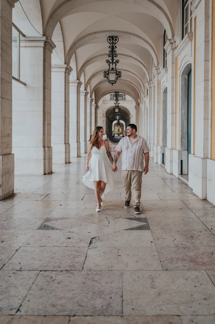 Hand in hand beneath the arcade | Lisbon couple photoshoot The couple walking towards the camera beneath the Praça do Comércio arcade during their couple photoshoot in Lisbon.