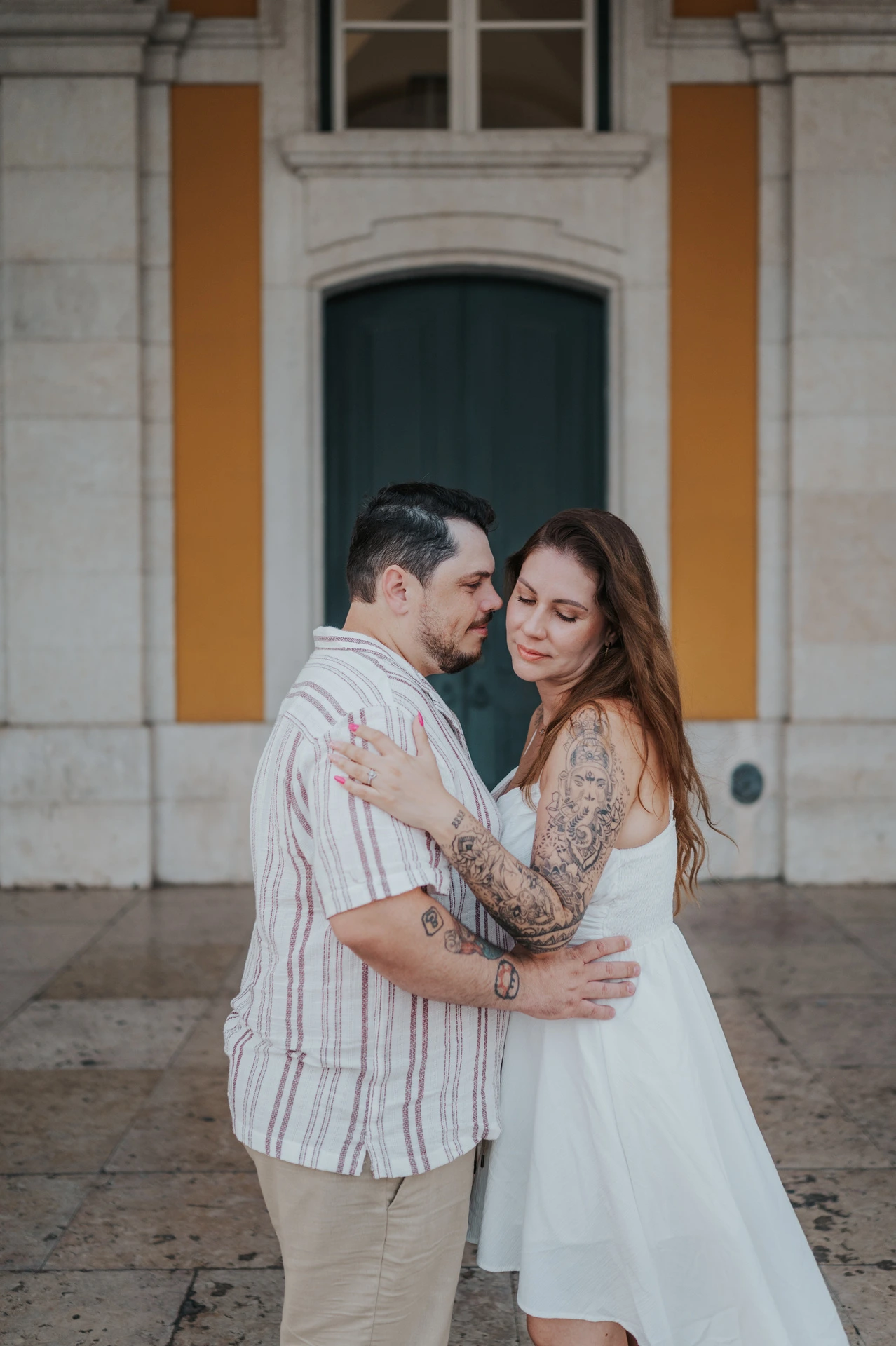The couple holding each other close beneath the stone arcade during their couple photoshoot in Lisbon.