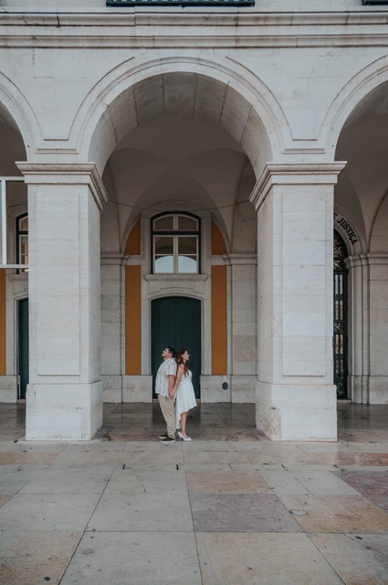 An embrace framed by the grand arch | Lisbon couple photoshoot The couple standing close together beneath the grand stone arch during their couple photoshoot in Lisbon.