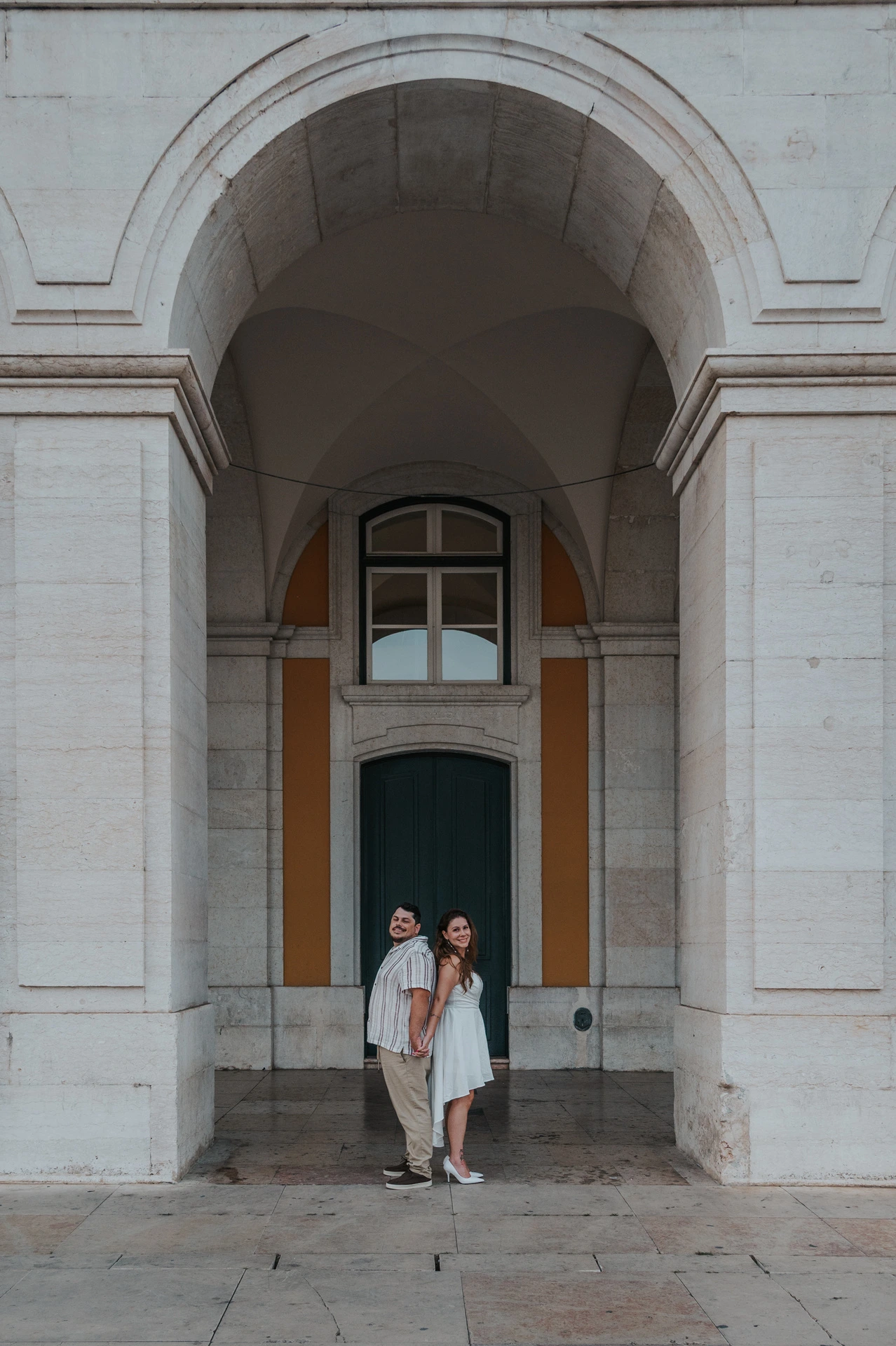 The couple standing together and looking upwards beneath the stone arch during their couple photoshoot in Lisbon.