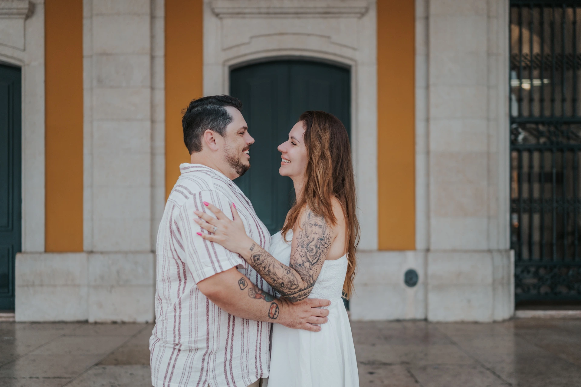 A close landscape portrait of the couple smiling at each other in an embrace beneath the arcade during their couple photoshoot in Lisbon.