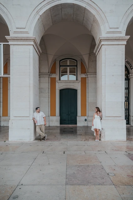 A portrait between the stone columns | Lisbon couple photoshoot The couple standing apart between the columns beneath the large stone arch during their couple photoshoot in Lisbon.