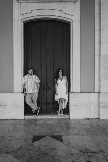 A doorway portrait in black and white | Lisbon couple photoshoot A black-and-white portrait of the couple standing on either side of a tall door at Praça do Comércio during their couple photoshoot in Lisbon.