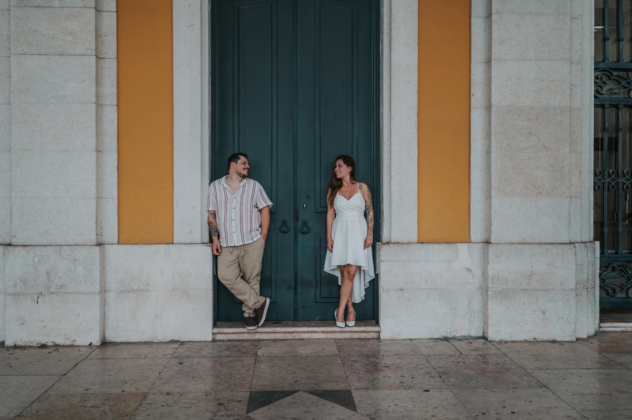 The green door and yellow facade | Lisbon couple photoshoot A wide photograph of the couple standing apart in front of the green door and yellow facade during their couple photoshoot in Lisbon.