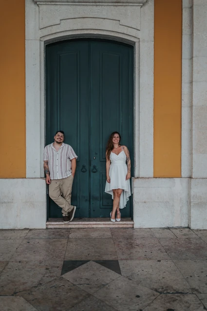 The couple leaning beside the green door in the yellow facade at Praça do Comércio during their couple photoshoot in Lisbon.