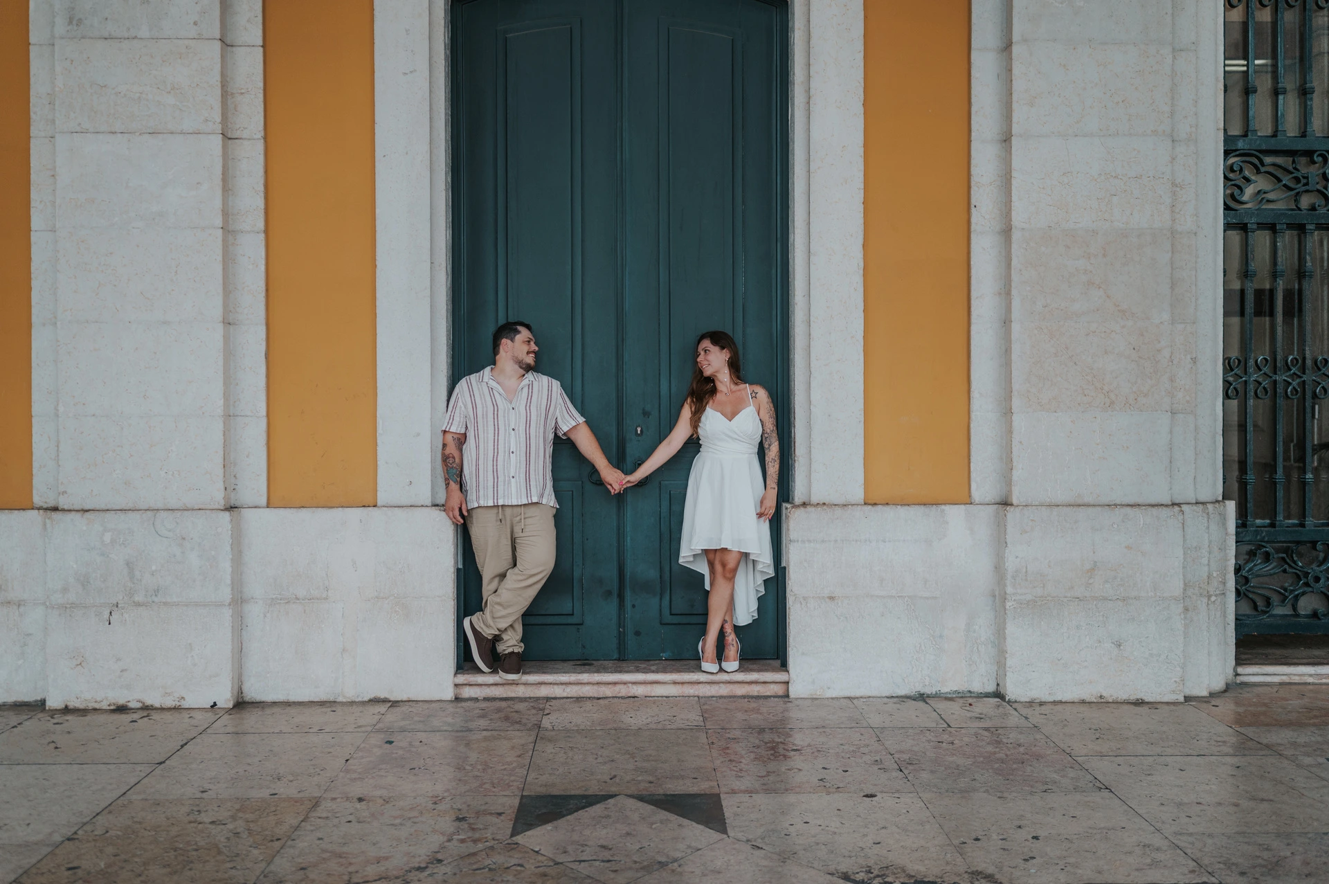 A wide portrait of the couple reaching towards one another in front of the green door during their couple photoshoot in Lisbon.