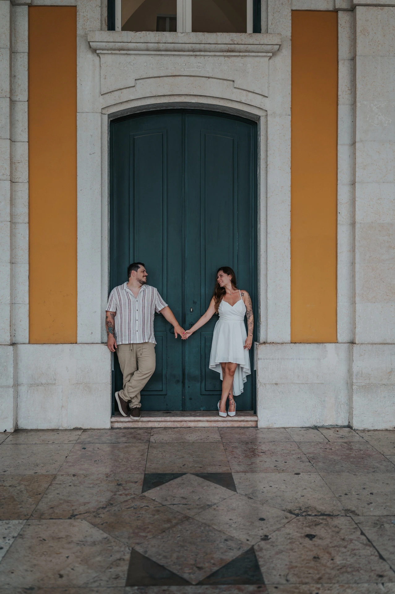 A vertical portrait of the couple holding hands and looking at each other in front of the green door during their couple photoshoot in Lisbon.