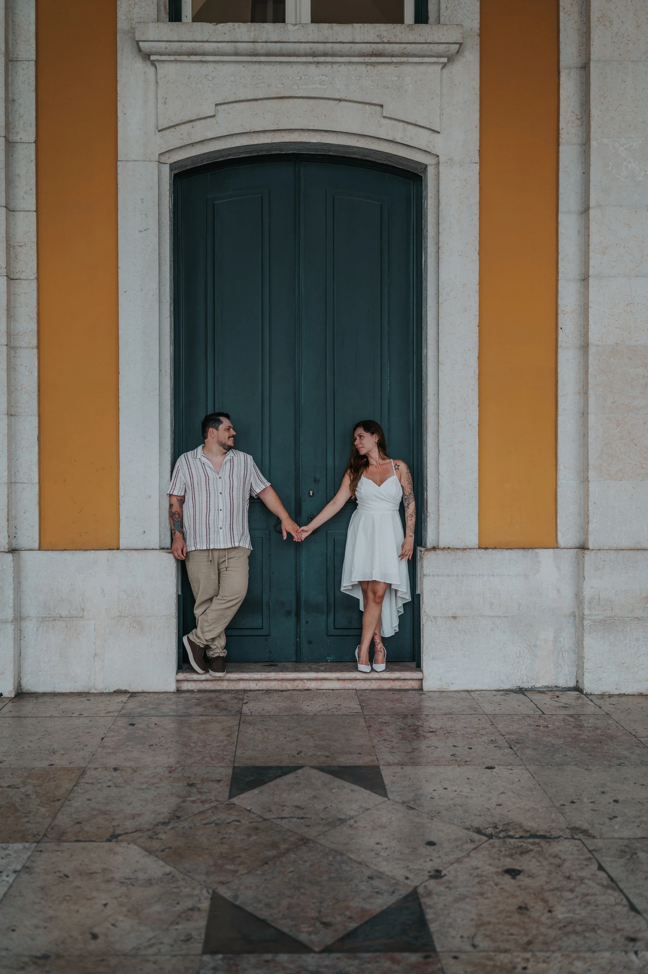 The couple reaching towards each other with hands joined in front of the green door during their couple photoshoot in Lisbon.