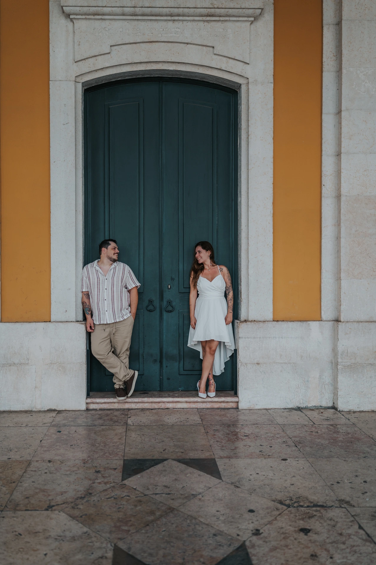 The couple looking across at one another beside the tall green door during their couple photoshoot in Lisbon.