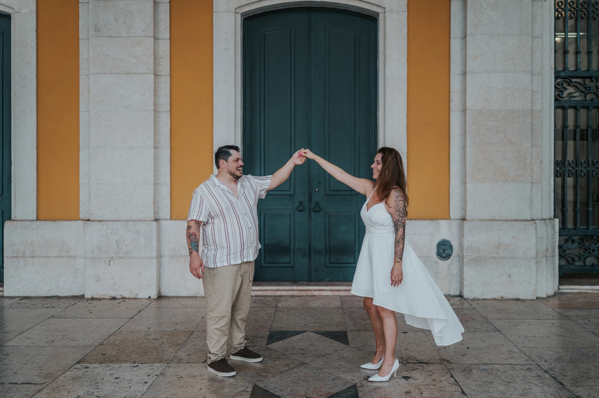 The couple raising their joined hands for a turn in front of the green door during their couple photoshoot in Lisbon.