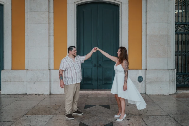 The couple raising their joined hands for a turn in front of the green door during their couple photoshoot in Lisbon.
