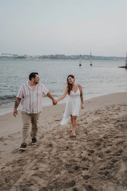 A smile on the riverbank | Lisbon couple photoshoot The couple smiling at each other as they walk along the sandy riverbank during their couple photoshoot in Lisbon.