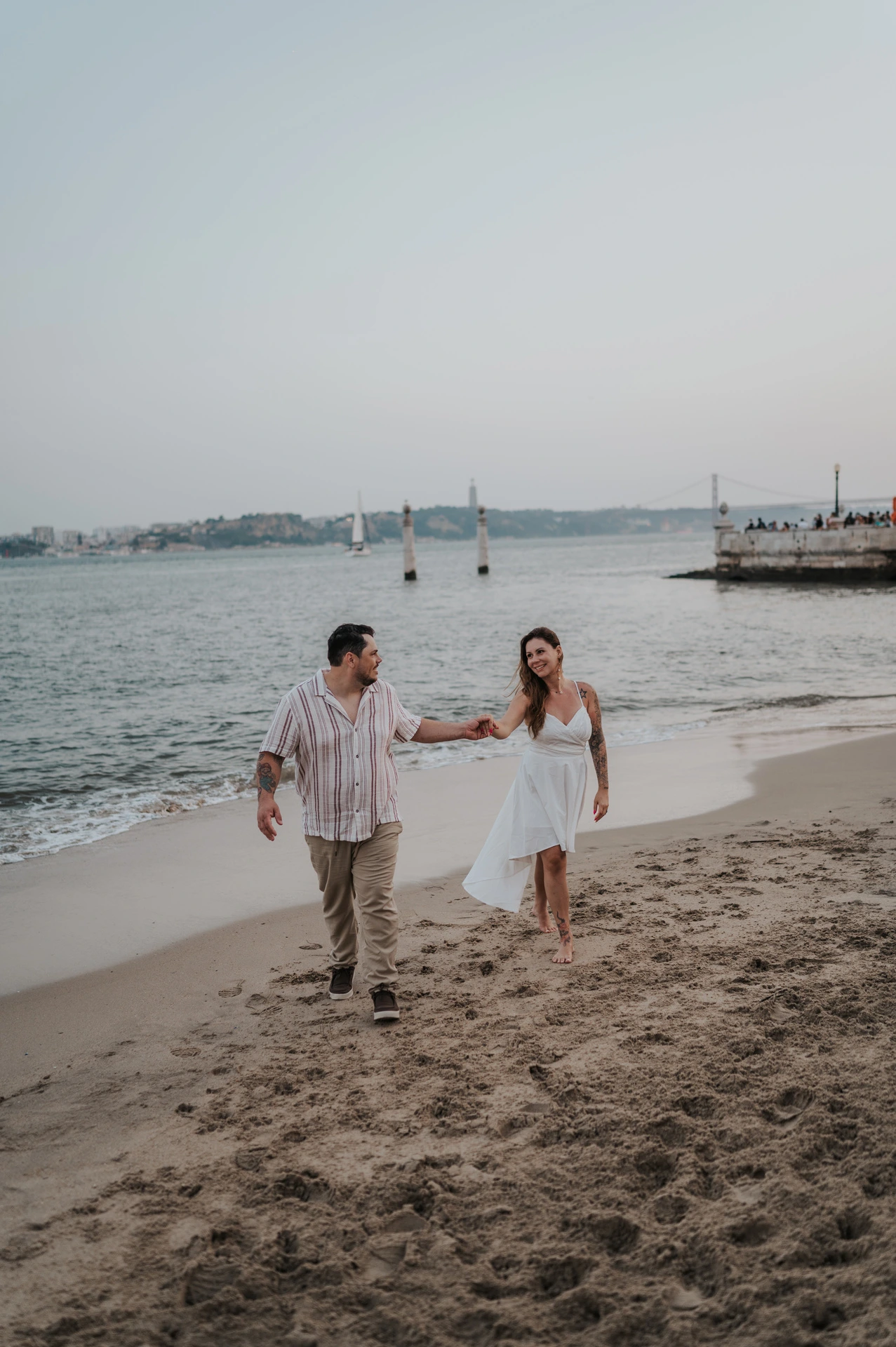 The couple walking hand in hand along the little beach beside the river during their couple photoshoot in Lisbon.