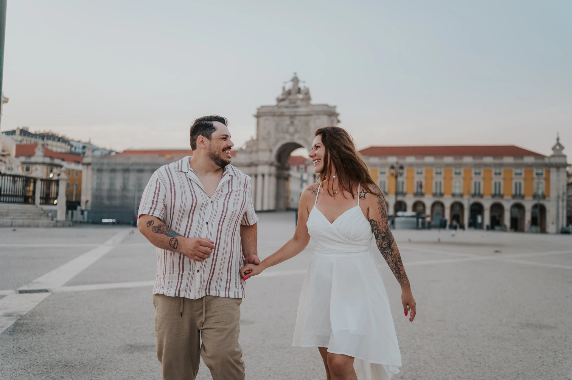 A wide portrait of the couple walking hand in hand with the yellow square behind them during their couple photoshoot in Lisbon.