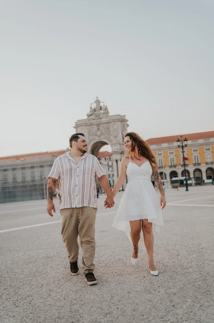 Hand in hand across the square | Lisbon couple photoshoot The couple walking hand in hand across Praça do Comércio with the large arch behind them during their couple photoshoot in Lisbon.
