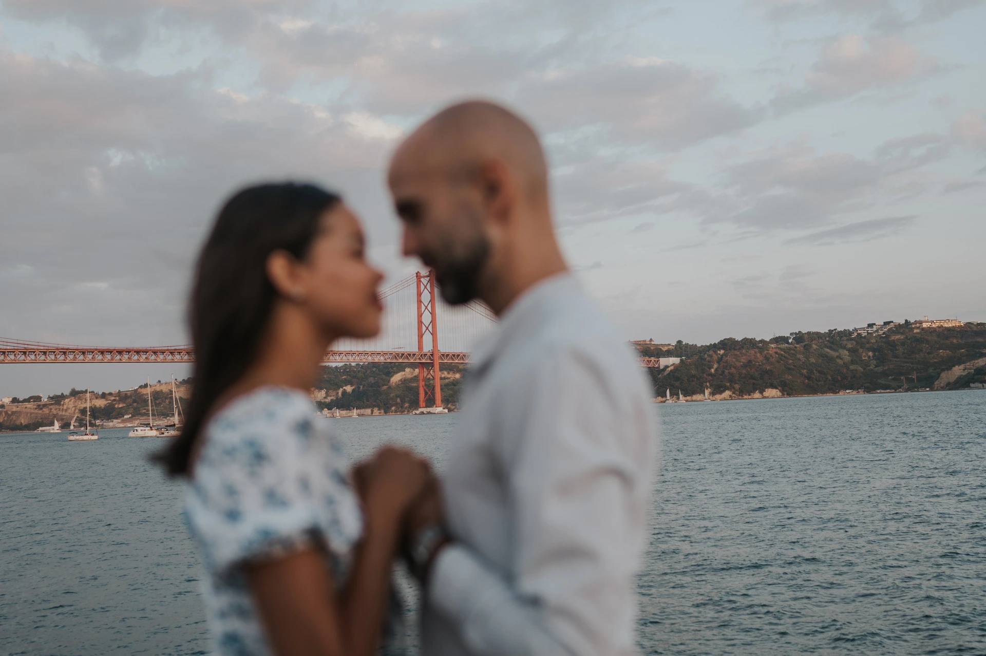 A softly focused portrait of the couple with the 25 de Abril Bridge behind them during their couple photoshoot in Lisbon.