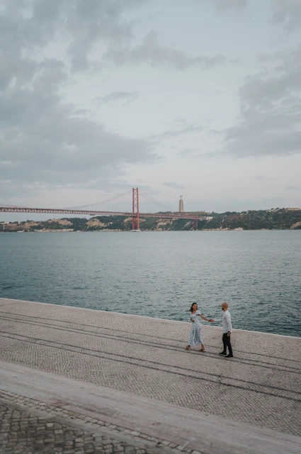 Reaching towards each other by the river | Lisbon couple photoshoot An elevated portrait of the couple reaching towards each other beside the river during their couple photoshoot in Lisbon.